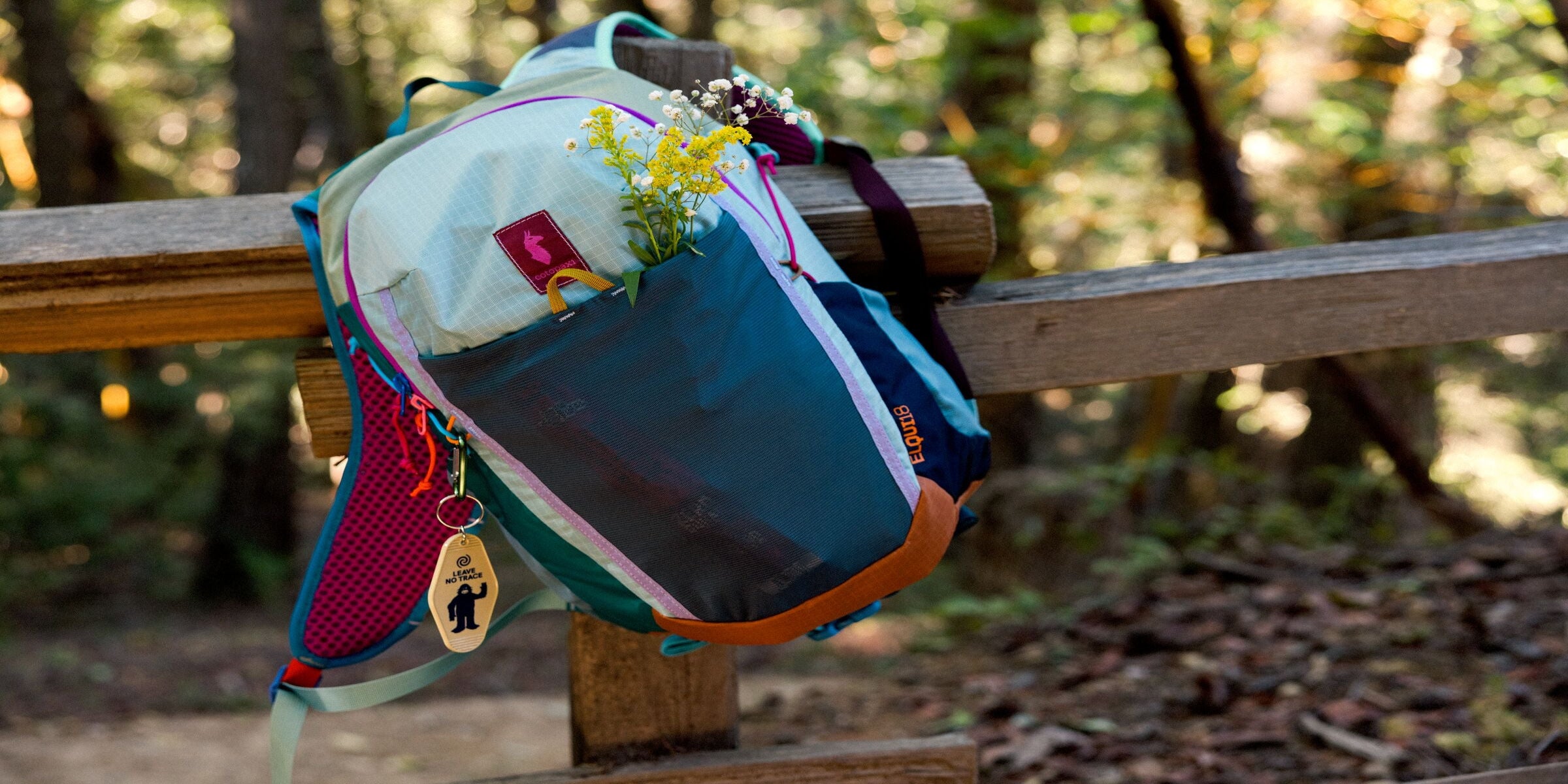 Colorful backpack with flowers on a wooden fence in a forest setting